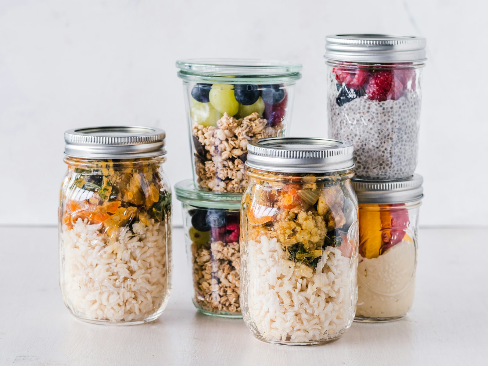 Tarros de vidrio con tapa llenos de arroz con verduras, avena, fruta y semillas de chía